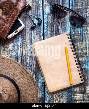 Vintage Paper journal with empty space for your text near travel hat, sunglasses and bag with smartphone on wooden table Stock Photo