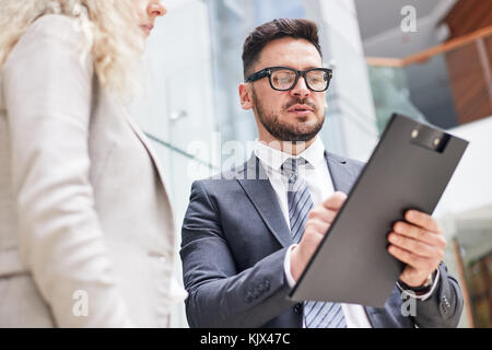 Handsome middle-aged manager showing results of accomplished work to female colleague while having working meeting at boardroom Stock Photo
