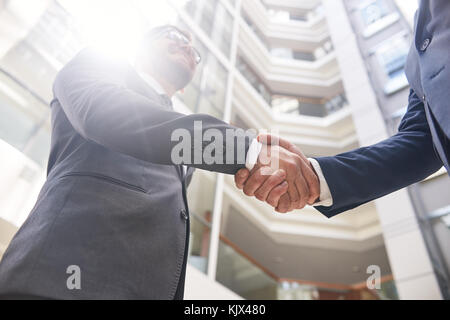 Low angle view of unrecognizable businessmen shaking hands after successful completion of negotiations, lens flare Stock Photo