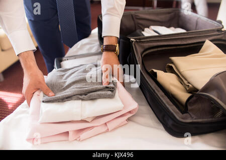 Close up of unrecognizable businessman packing suitcase for business trip folding clothes on hotel bed Stock Photo