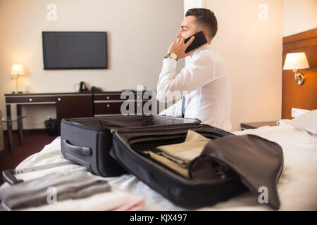 Rear view portrait of successful businessman speaking by phone after arriving to hotel while unpacking luggage Stock Photo