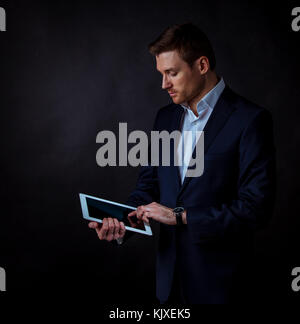 Young handsome businessman using digital tablet, studio shot on dark background Stock Photo