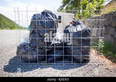 Black garbage bag garbage dump, bin,trash, garbage, rubbish, plastic bags pile background , Cage garbage bin with black garbage bags. Stock Photo