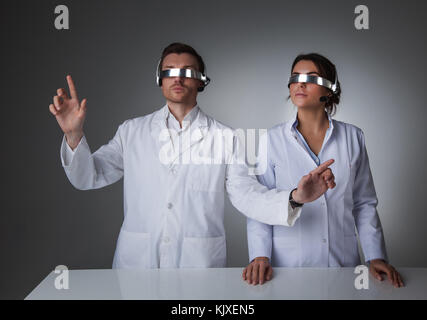 Two scientists or doctors using futuristic VR goggles headset with microphone and touching virtual screen Stock Photo
