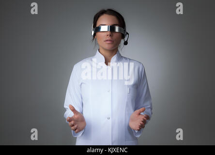 Female scientist or doctor using futuristic VR goggles headset with microphone and holding virtual object Stock Photo