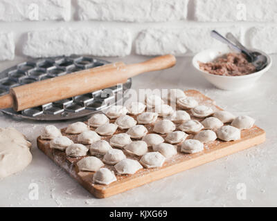 Uncooked russian pelmeni on cutting board and ingredients for homemade pelmeni on white table. Process of making pelmeni, ravioli or dumplings with me Stock Photo