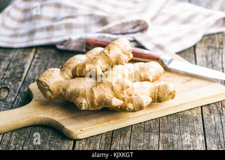 A healthy ginger root on a cutting board lying on an old wooden table. Food concept. Stock Photo