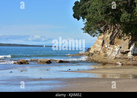 Marginal oceanic surf on flat beach with rocky cliff on th side. Stock Photo