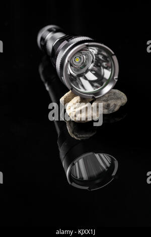 Flashlight LED on stones mirroring on black background. Useful for adventure, military, hunting, outdoor, protection, security, background Stock Photo