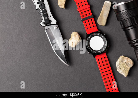 Hunting objects, folding hunting knife , red smartwatch and black flashlight on black background, Useful for adventure, military, hunting, outdoor, pr Stock Photo