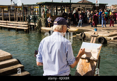 An unknown artist paints the scene as travellers leave a Vaporetto (Water Bus) stop beside Ponte della Paglia in Venice on September 13, 2017. Stock Photo