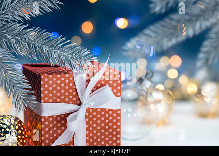 christmas decorations with red gift box and fir tree branches on blurred garland lights background Stock Photo