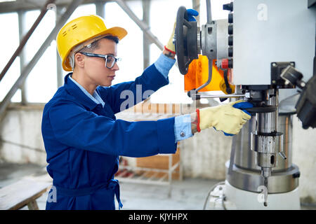 Serious confident female manual worker in hardhat wearing workwear adjusting drilling machine before operation Stock Photo