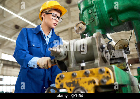 Concentrated attractive young factory operator in hardhat setting machine and preparing for work with equipment Stock Photo