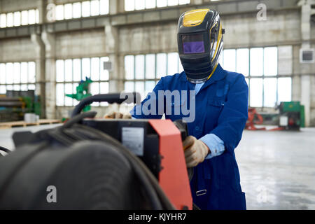 Unrecognizable welder in helmet working on industrial machine in factory Stock Photo