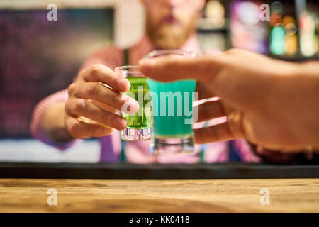 Close up of two male hands holding colorful alcohol shots at bar counter and clinking small glasses toasting in celebration Stock Photo