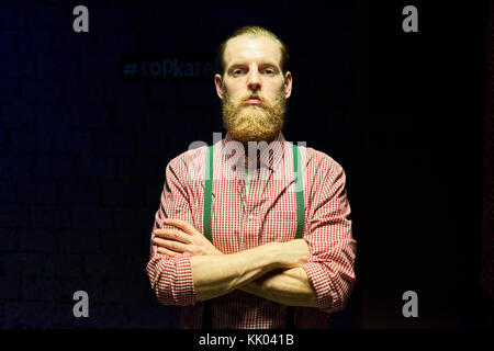 Portrait of handsome bearded hipster posing confidently with arms crossed against black background drowning in harsh contrasted spot light from above Stock Photo