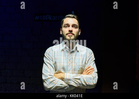 Portrait of handsome young man posing confidently with arms crossed against black background drowning in harsh contrasted spot light from above Stock Photo
