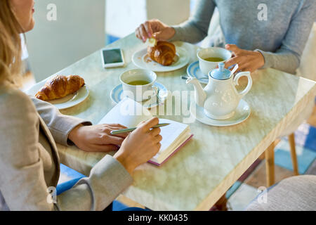High angle view of two unrecognizable young women meeting during lunch break at cafe table with tea and croissants Stock Photo