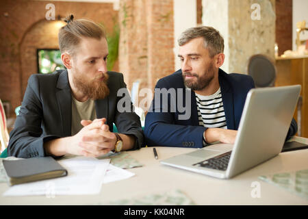 Confident bearded business partners discussing details of mutually beneficial cooperation while gathered together at modern restaurant Stock Photo