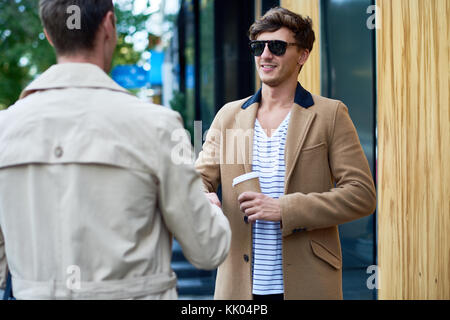 Portrait of two handsome young businessmen wearing autumn coats chatting outdoors in city streets, copy space Stock Photo