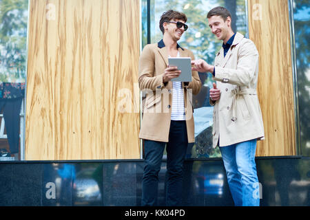 Portrait of two handsome young businessmen wearing autumn coats using digital tablet and chatting outdoors in city streets, copy space Stock Photo