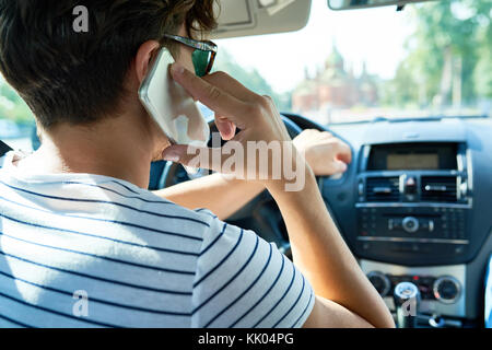 Rear view of young man driving luxury car and speaking by smartphone, copy space Stock Photo