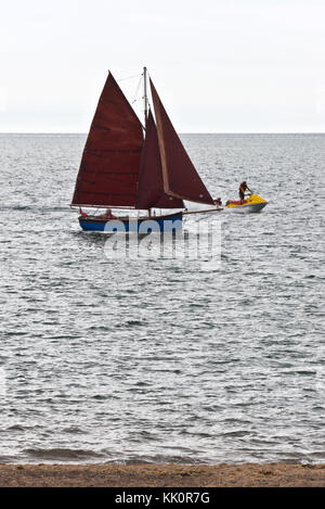 A lone yachtsman sailing into the entrance of the River Exe at Exmouth on the south Devon Coast on a calm summers day with all his sails up Stock Photo