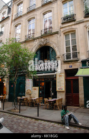 Man sitting on a pavement in front of a small bistro in Paris writing or drawing something Stock Photo