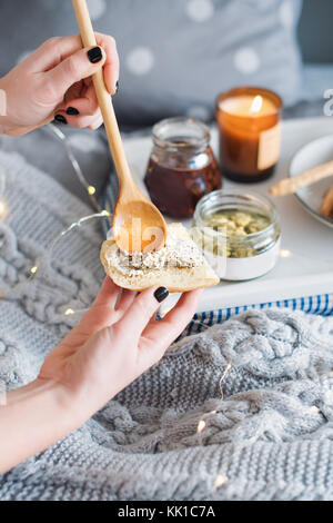 Female hands smearing cream cheese on fresh bread. Breakfast in bed, a tray with cheese, grissini, jam and aromatic candle. Christmas morning. Honeymo Stock Photo