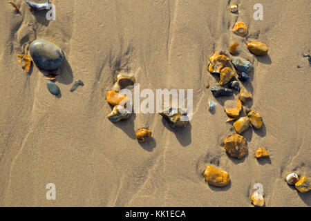 Pebbles left by the tide on a sandy beach, viewed from above and photographed in landscape format. Stock Photo