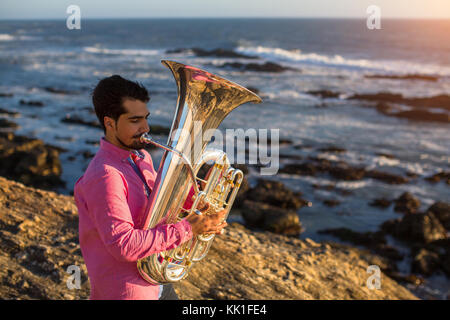 Young musician playing the trumpet on the ocean coast. Stock Photo