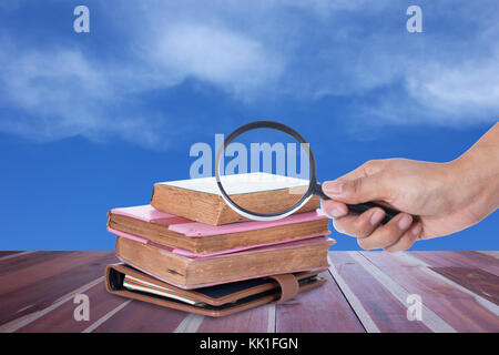 Hand holding magnifying glass over book with blue sky Stock Photo