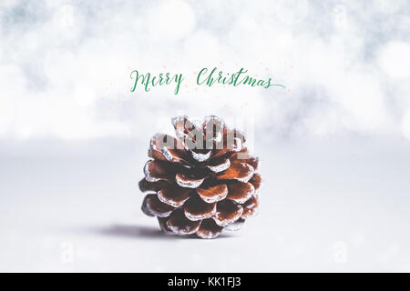 Green Merry Christmas and sparkling star with brown pine cone on white table and silver bokeh light blur background,Holiday Greeting card Stock Photo