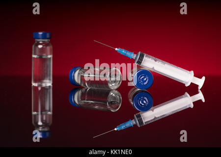 Syringe and medical vials isolated on red dark background with glossy reflection Stock Photo