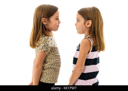Identical twin girls are looking at each other and smiling. Concept of family and sisterly love. Profile side view of sisters looking at each other. Stock Photo