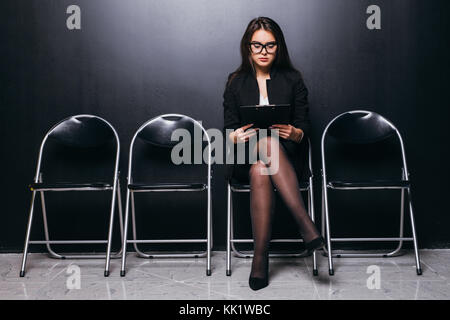 People, employment and recruitment. Charming unemployed woman in glasses smiling broadly having confident look before job interview, sitting on chair  Stock Photo