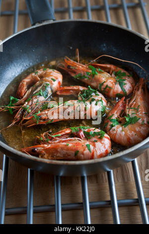 Pan fried king prawns in shells with garlic and herbs in black frying pan on steel grill. Portrait format. Stock Photo