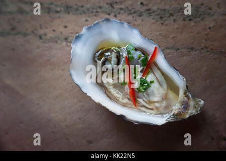 Fresh oyster in half shell with red chilli and herbs on stone base Stock Photo