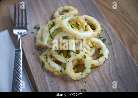 Cooked squid rings with light batter, lemon and herbs served on stone tablet Stock Photo