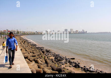 Man and people walking along side marine drive, long shot with sea and buildings, Mumbai Stock Photo