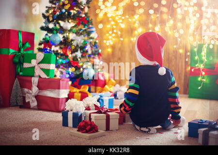 Boy and sitting on the floor with presents near christmas tree Stock Photo