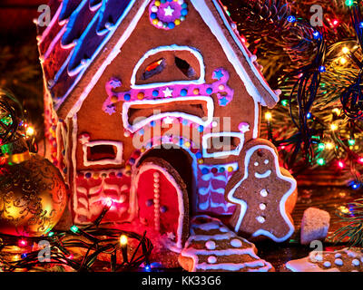 Ginger bread houses with Christmas garland. Xmas food gingerbread man cookies decorating holiday table burning candles. Gingerbread trees lay on table Stock Photo