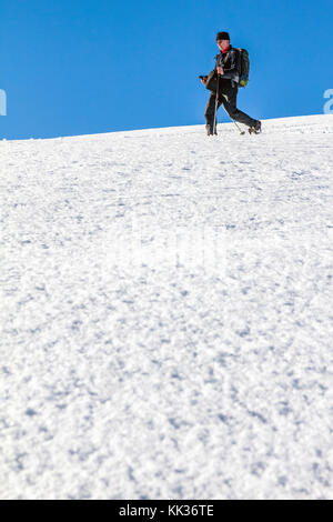 Man is snowshoe hiking through deep snow on sunny day Stock Photo
