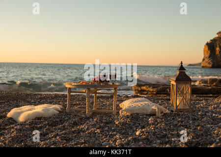 Romantic outdoor dinner with wine and cheese by seaside. Two glasses of wine, grapes, dried fruits and cheese placed on small round table, with white  Stock Photo