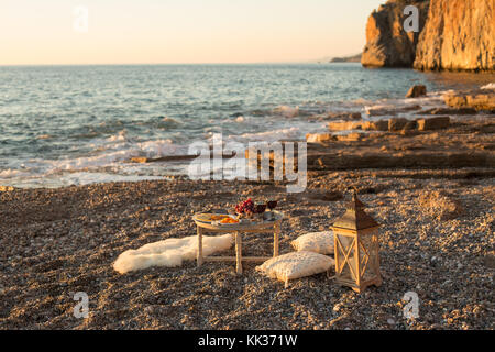 Romantic outdoor dinner with wine and cheese by seaside. Two glasses of wine, grapes, dried fruits and cheese placed on small round table, with white  Stock Photo