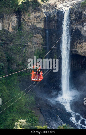 Ecuador, Tunguragua - November 27, 2017: Tourists gliding on the zip line trip against Bridal veil (Manto de la novia), waterfall in Cascades route, B Stock Photo