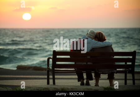 Romantic elderly couple on a bench watching the sunset over the Mediterranean sea in Tel Aviv. Stock Photo