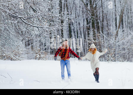 Cheerful running couple along the forest covered with snow during the snowfall. Stock Photo