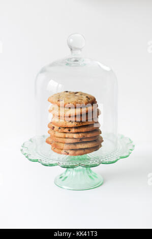 Stack of freshly baked, homemade  traditional American Chocolate Chip Cookies on glass cake stand on white background Stock Photo
